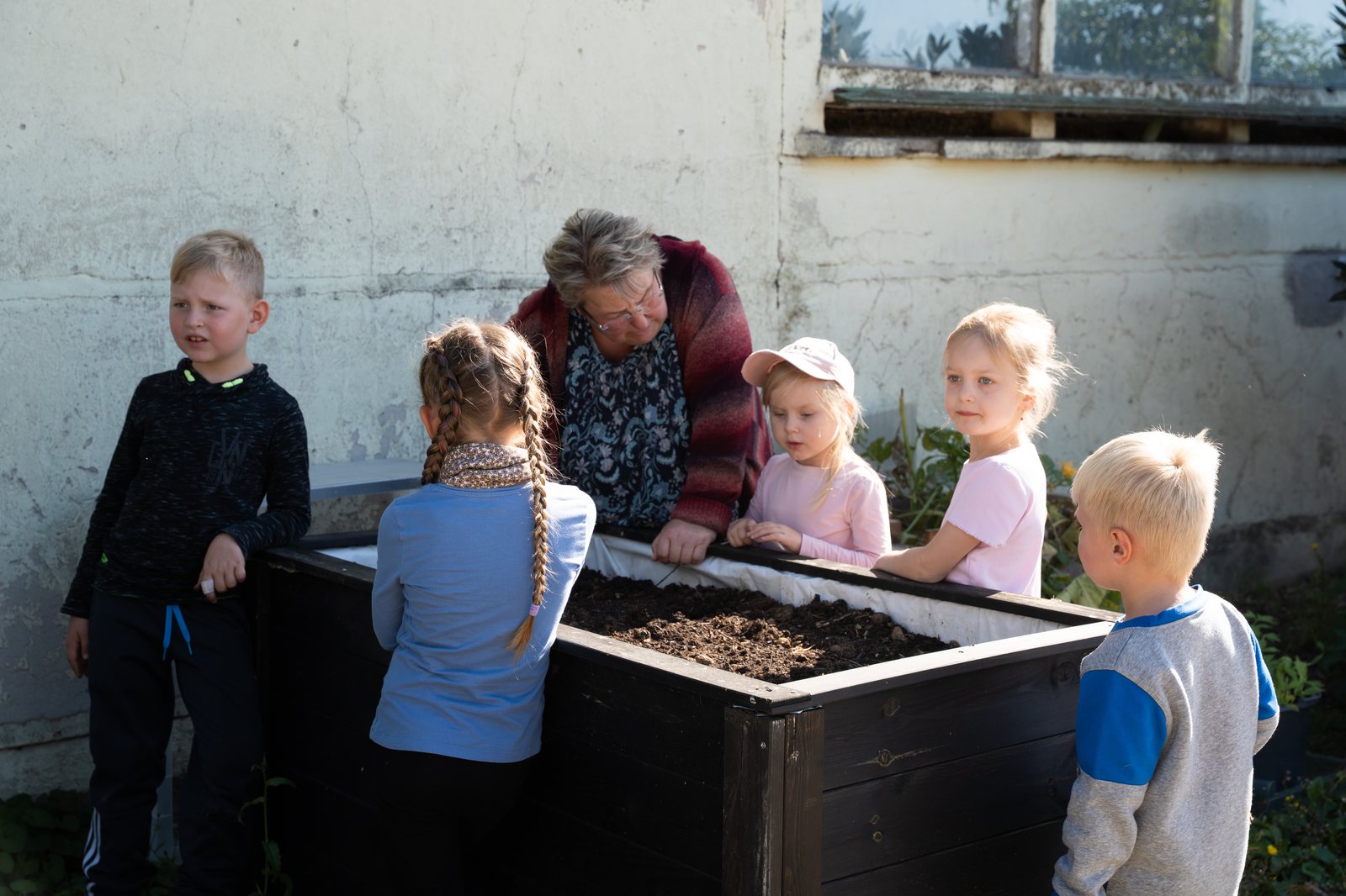 Kinder und eine Erwachsene arbeiten gemeinsam an einem Hochbeet.