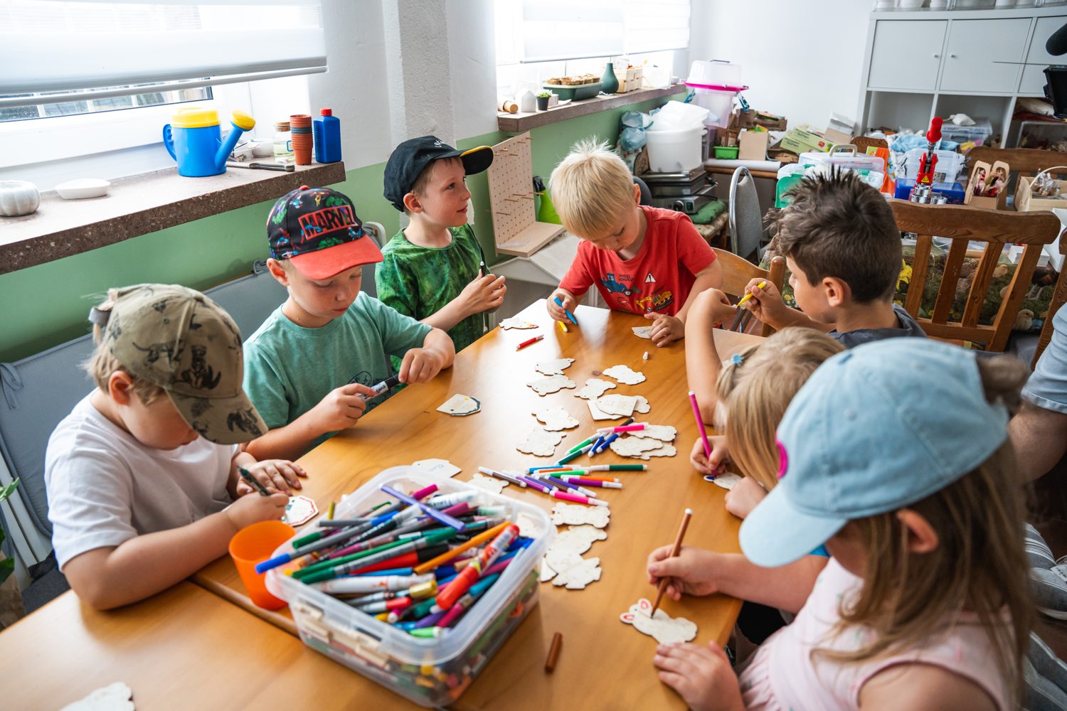 Kindergruppe bemalt am großen Tisch im Aufenthaltsraum kleine Holzfiguren